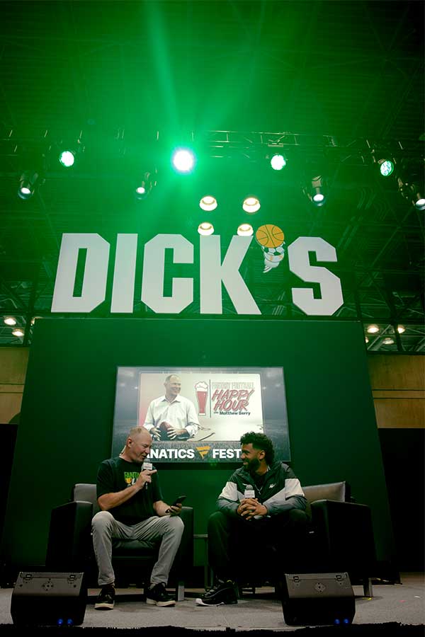 image of two men talking on a stage with the Dick's Sporting Goods logo behind them and green lights