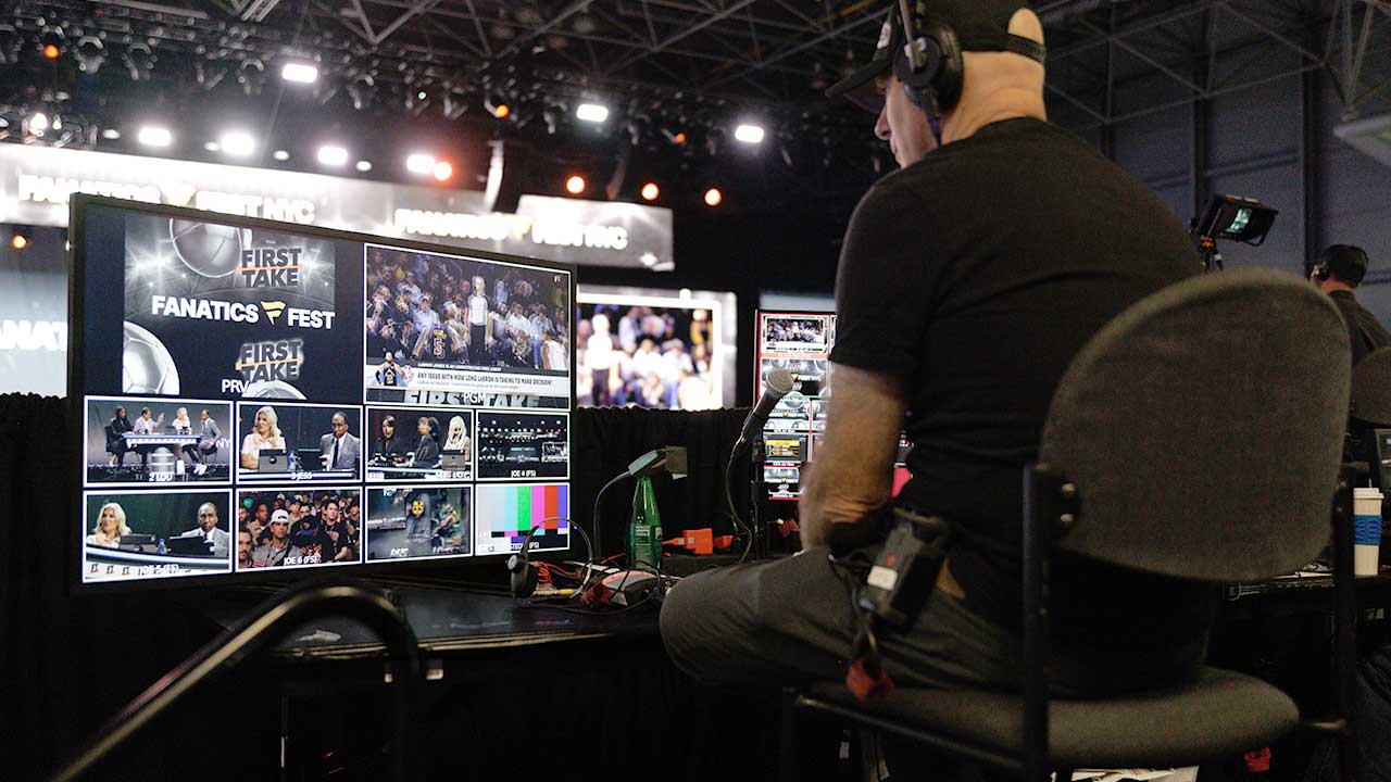 Image of crew members working while facing the stage watching a monitor of all the video feeds from the camera
