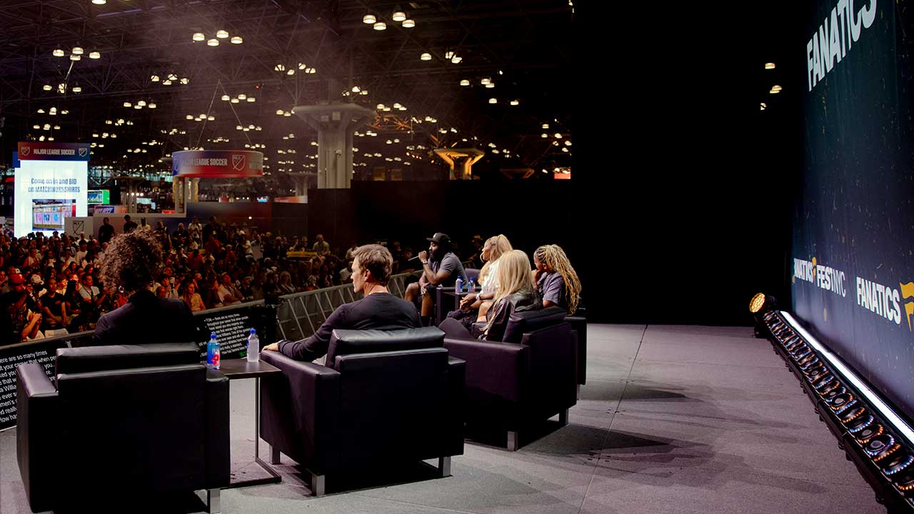 Image from behind a panel of seated speakers looking out into the crowd from stage