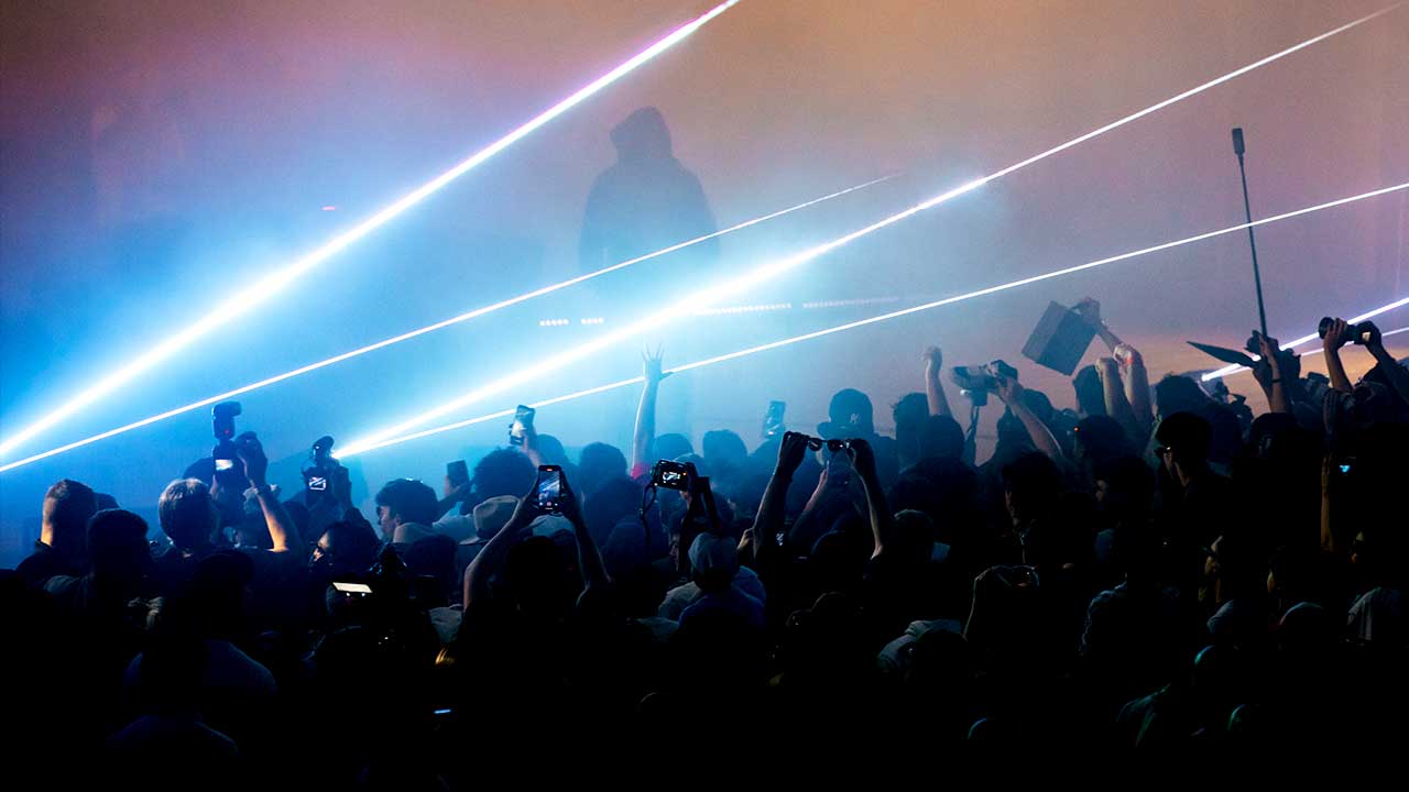 Image of performer on stage with beams of laser light going out in the crowd and fans recoding the moment with their cell phones 